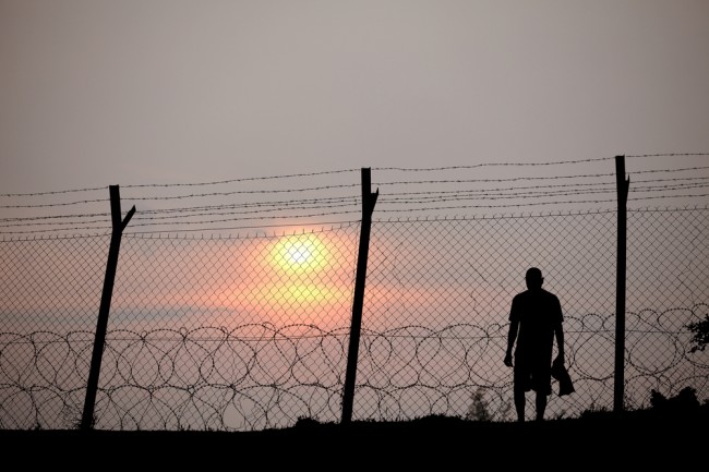 Zdjęcie Silhouette of a prisoner behind a barbed wire fence in a concentration camp against fiery setting sun. pochodzi z serwisu ShutterStock